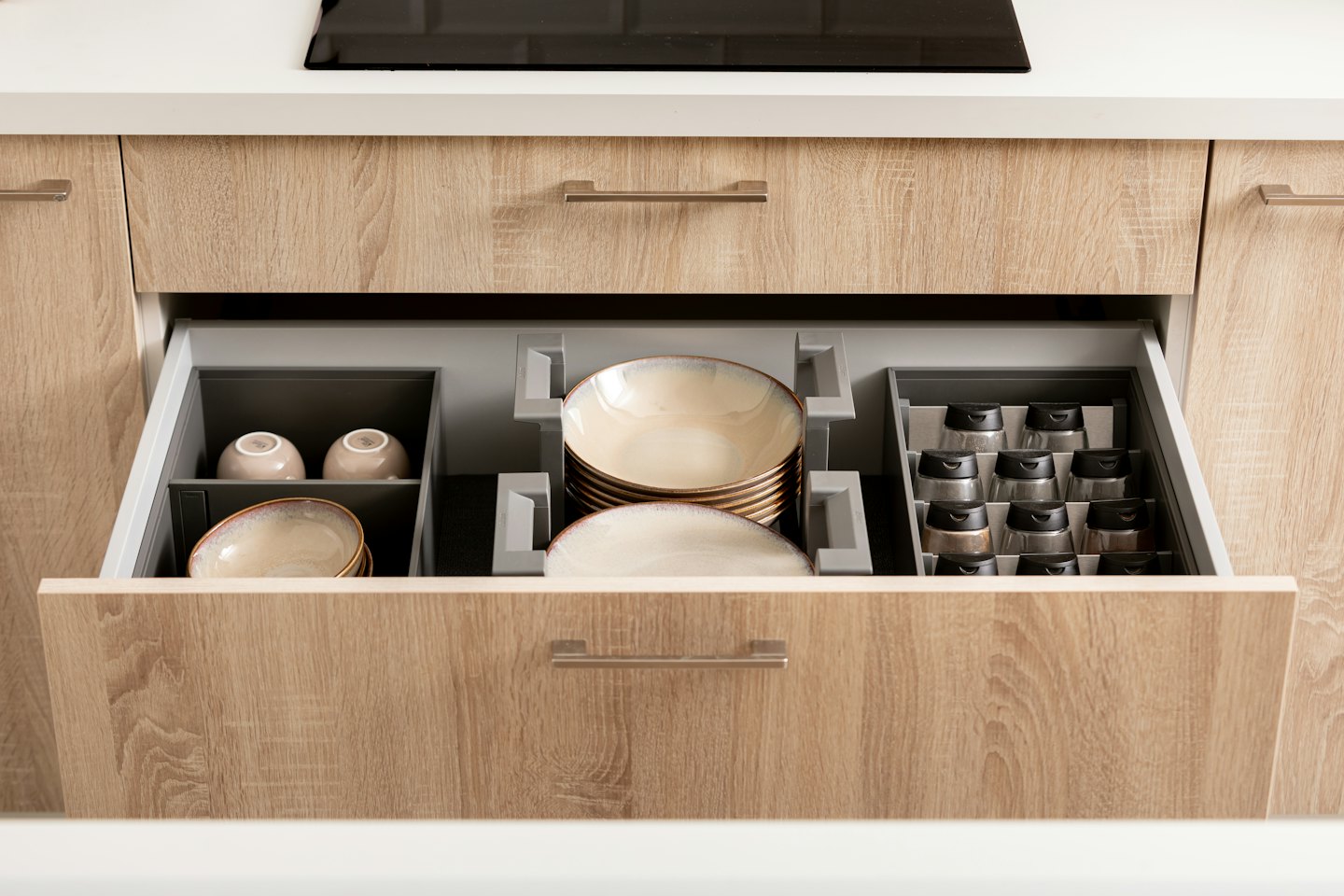 Open kitchen drawer with organized dishes and spice jars.
